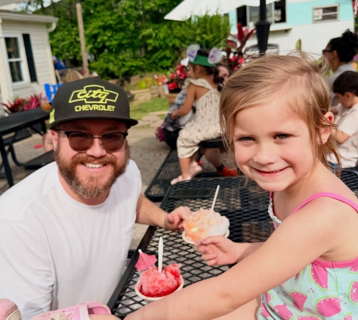 A dad and his daughter smiling with shave ice at the picnic tables