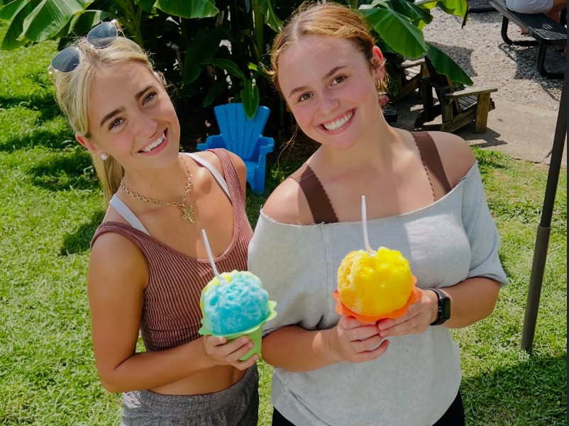 Two friends holding blue and yellow shave ice on the grass